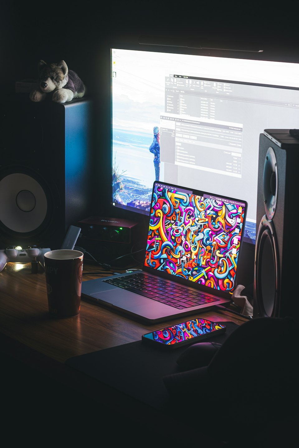 Laptop, monitor, altoparlanti e tazza di caffè su una scrivania.