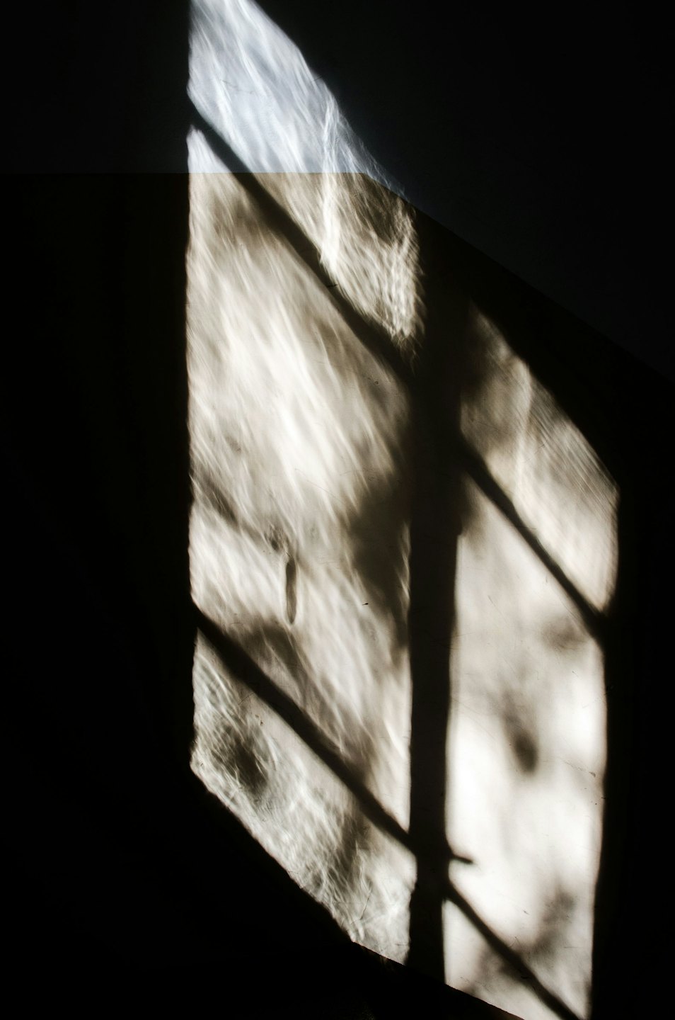 La luce del sole crea motivi geometrici su una superficie scura e ruvida.